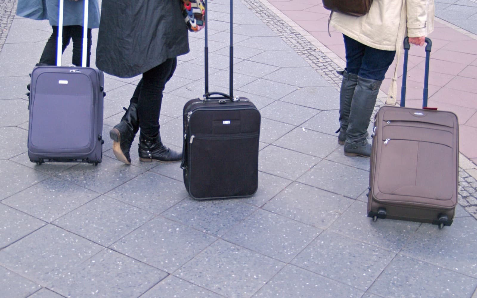 Three soft-shell wheeled cabin cases, handles extended, on a station forecourt