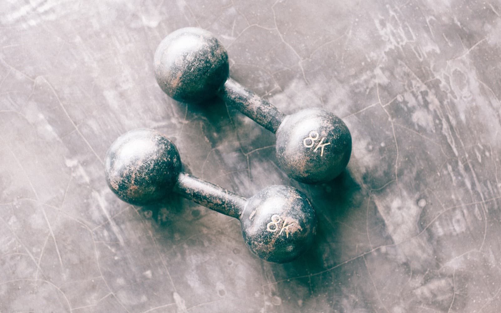 Two worn cast-iron ball-end dumbbells marked 8K lying side by side on a scuffed grey concrete floor