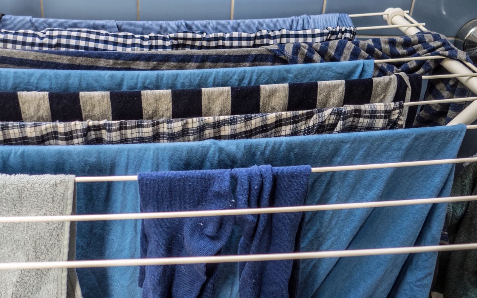 Blue and checked shirts and towels hung to dry across the rails of a folding indoor drying rack