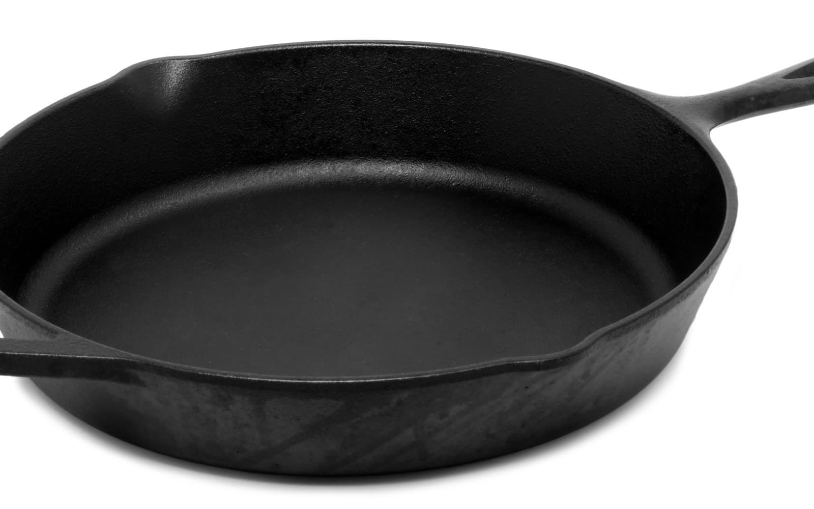 A bare black cast iron skillet with pour spouts and a long handle, photographed from above on white