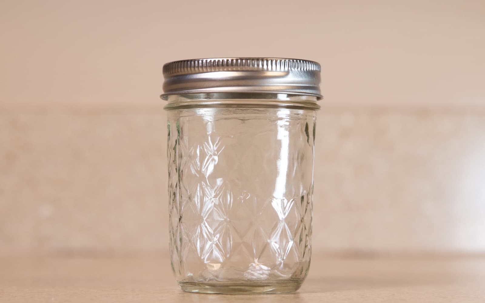 An empty quilted glass storage jar sealed with a plain metal screw lid, standing on a wooden worktop
