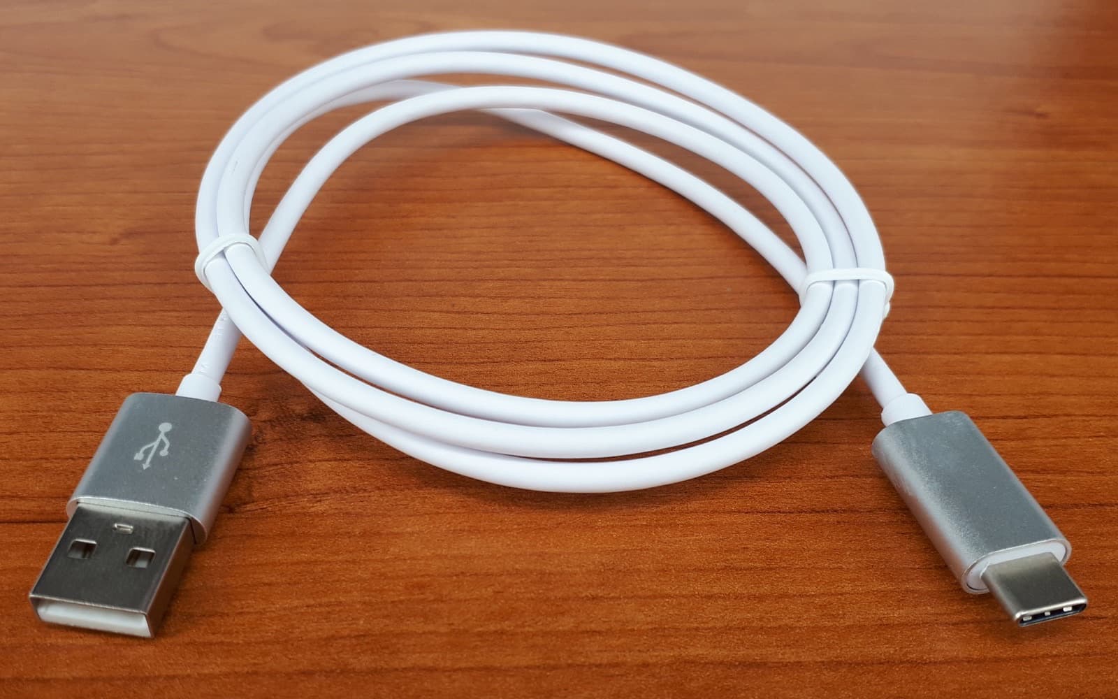 A coiled white cable on a wooden desk, a metal-shelled USB-C plug at one end and a flat USB-A plug at the other